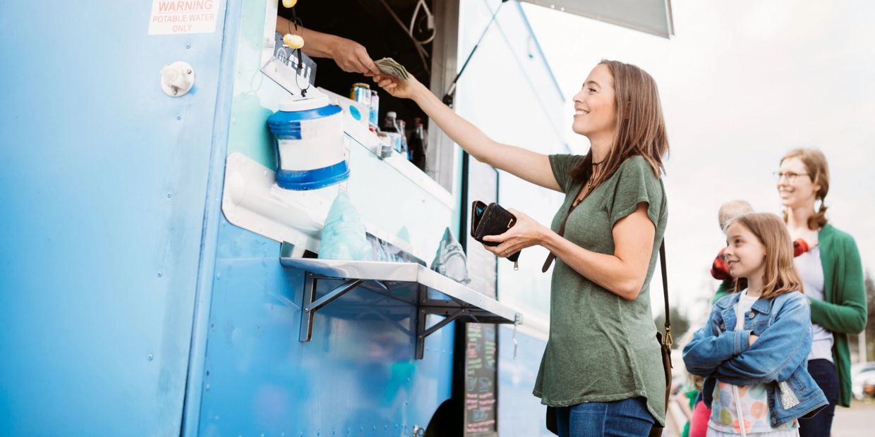 Woman buying food from a food truck. A child is standing next to her and a line of people behind.