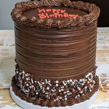 Tall chocolate birthday cake with sprinkles.
