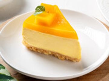 A slice of mango cheesecake garnished with fresh mango and mint.