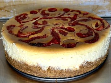 A creamy cheesecake with a swirled raspberry topping on a graham cracker crust.