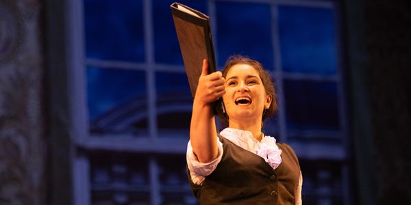 Elena, a Jo March in Little Women, holds a folio aloft