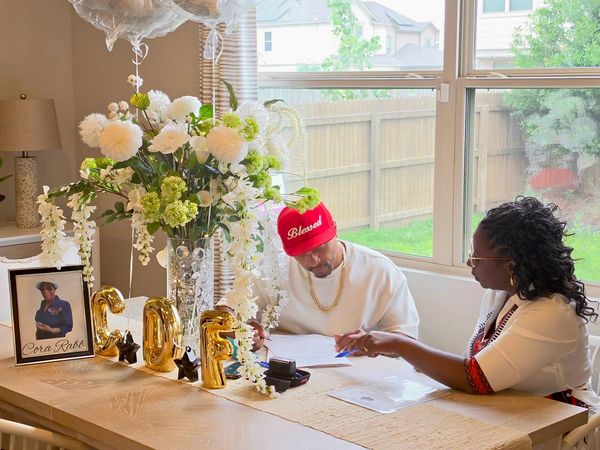 Two people signing documents at a decorated table with flowers and gold balloons.