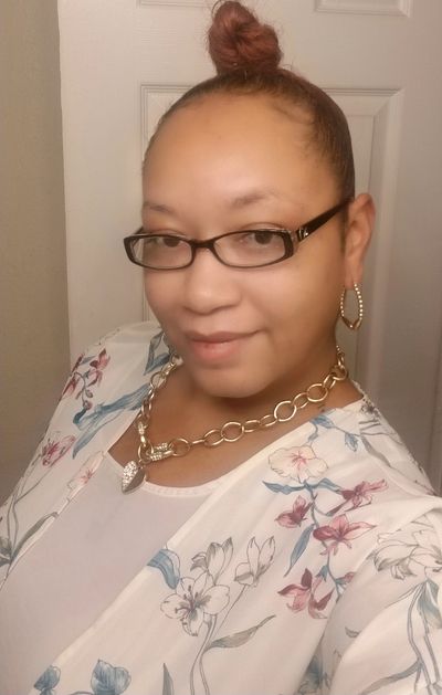 Woman with glasses and floral top smiling.