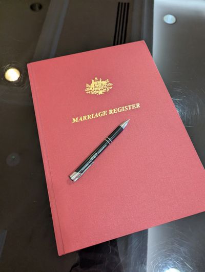 A red marriage register book with a pen on a reflective surface.