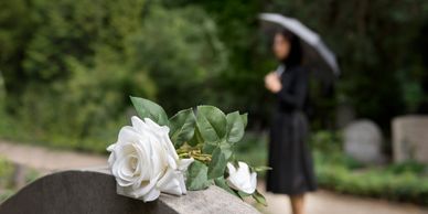 White roses placed on a gravestone with a mourner in the background.