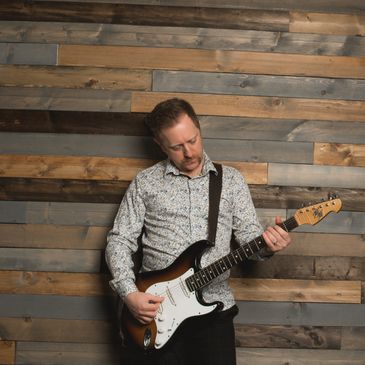 Man playing electric guitar against a wooden wall.