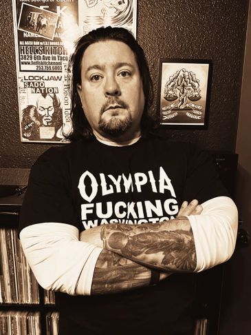 Man with tattoos wearing a bold Olympia Washington t-shirt.