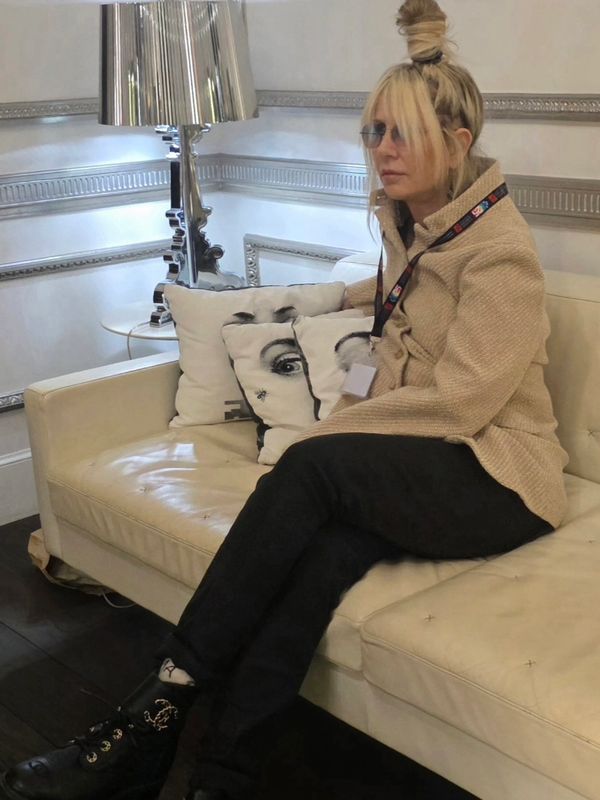 Woman with sunglasses sitting on a cream leather couch with artistic face pillows.