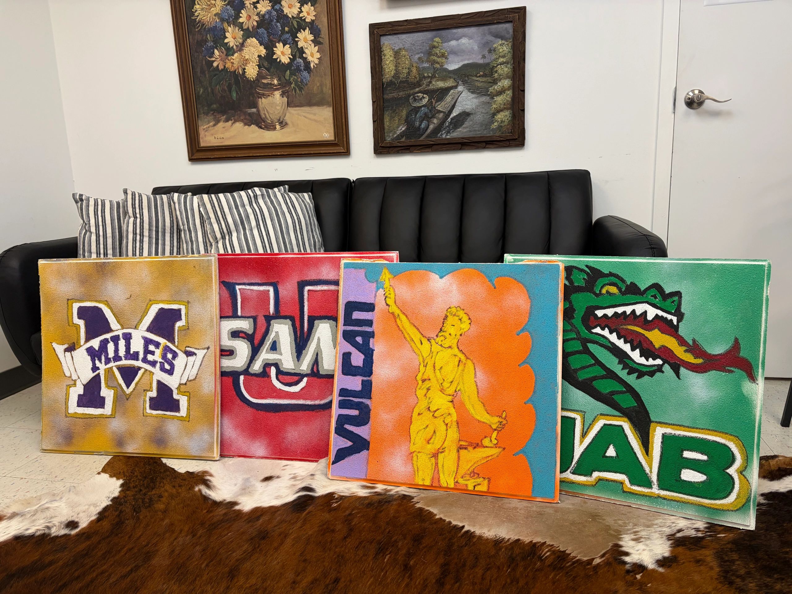 Colorful art paintings leaning against a black sofa indoors.