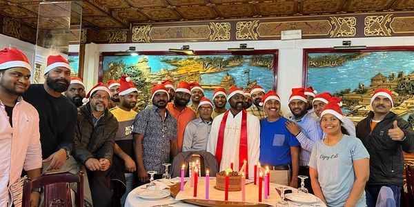 Group of people wearing Santa hats celebrating with a cake and candles indoors.