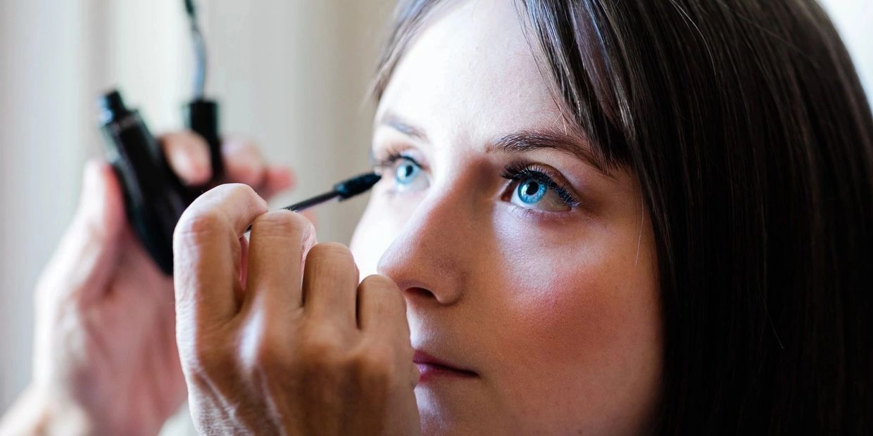A woman applying mascara to her eyelashes with a focused expression.