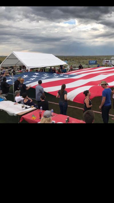 People holding a large American flag outdoors under a cloudy sky.