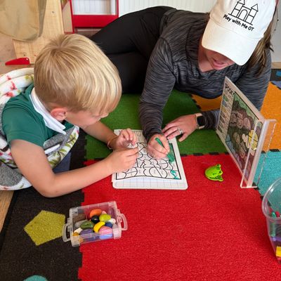 A child and adult collaborate on a drawing activity on a colorful carpet.