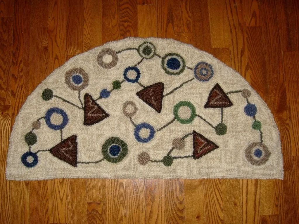 Semi-circular rug with geometric patterns on a wooden floor. Hand hooked by Rose Wilson.