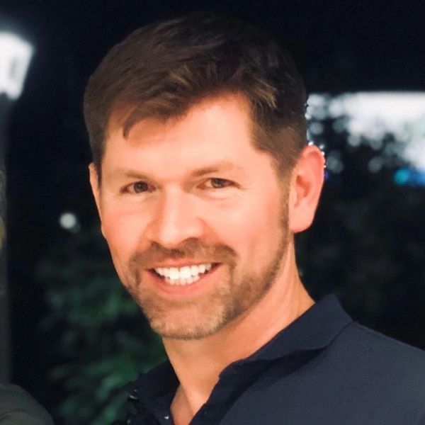 Smiling man with short brown hair and a beard in a dark shirt.