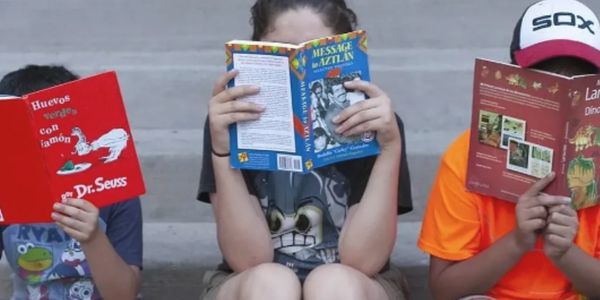 Three children sitting and reading different books, faces hidden behind covers.