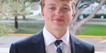 Young man in a suit and tie smiling outdoors.