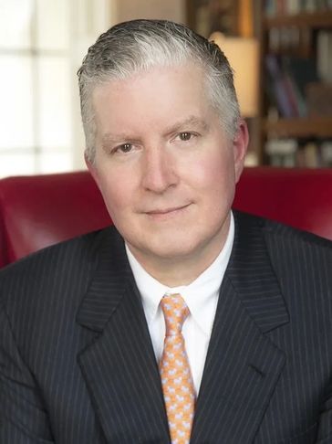Professional man in a suit and orange tie seated in a red chair.