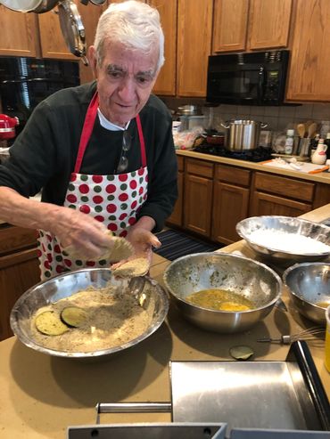 Elderly man breading eggplant slices in kitchen.