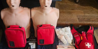 Two CPR manikins with red emergency bags and medical supplies.
