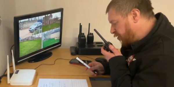 Man communicates on walkie-talkie in front of security monitor.