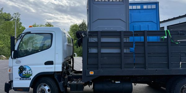 White truck carrying portable toilets parked outdoors.