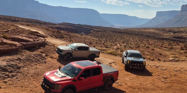 Three trucks on a rocky, desert trail under a blue sky.