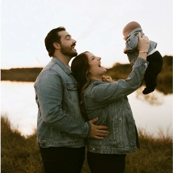 family smiling and holding up their newborn