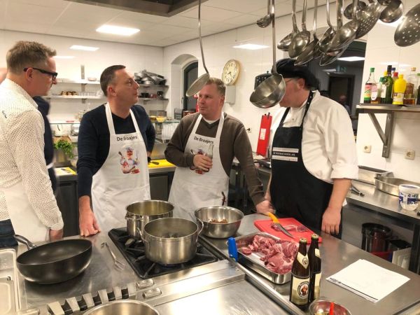 Vier Männer in einer professionellen Küche diskutieren beim Kochen.