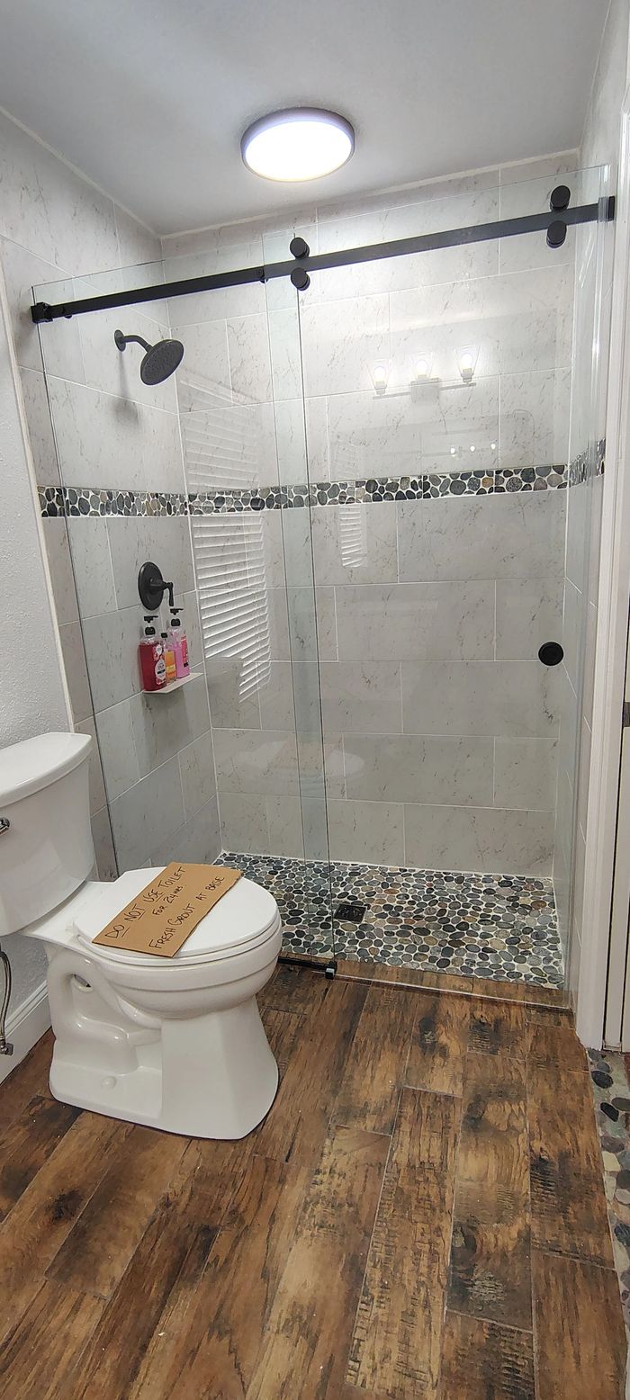 Modern bathroom with glass shower and wooden floor.