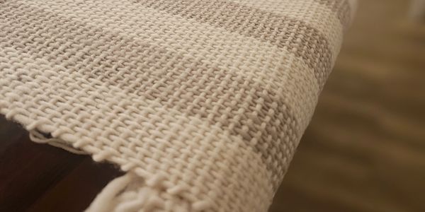 Close-up of a woven beige and white striped textile on wooden frame.