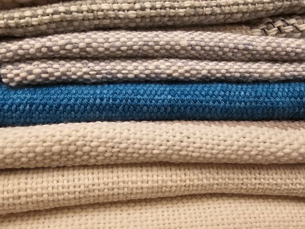 Close-up of stacked knitted and woven fabrics in neutral tones with a blue accent.