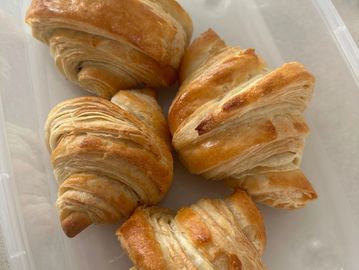 Four golden-brown croissants in a plastic container.
