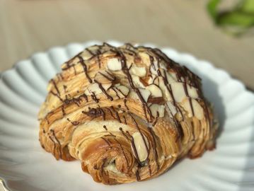 Almond croissant drizzled with chocolate on a white plate.