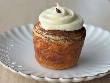 A cinnamon roll topped with cream and a coffee bean on a white plate.