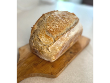 Freshly baked loaf of crusty bread on a wooden cutting board.
