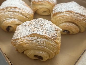 Four chocolate croissants dusted with powdered sugar in a box.