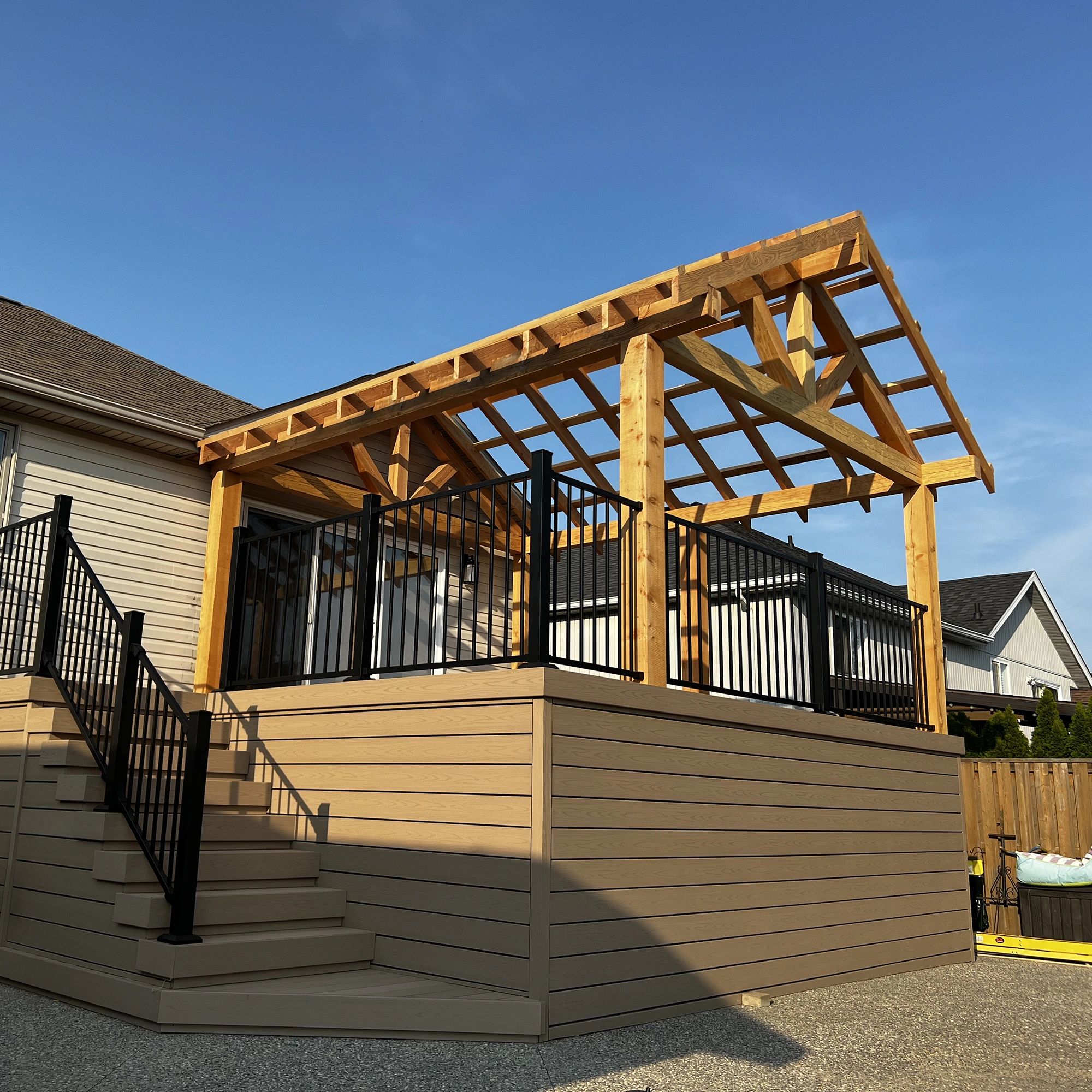 A raised wooden deck with black metal railings and an unfinished pergola frame.
