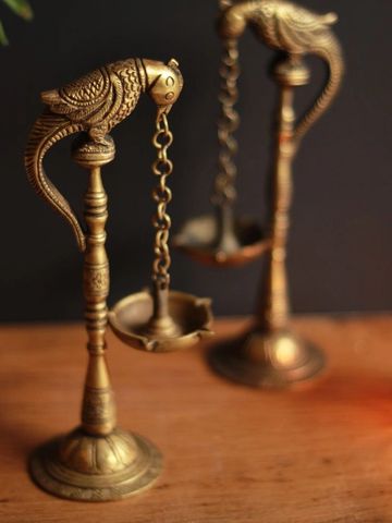 Intricately designed brass oil lamps shaped like parrots, placed on a wooden surface.