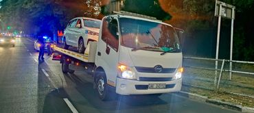 White MHD Transport Truck towing a white SUV in the road Infront of a traffic officer.