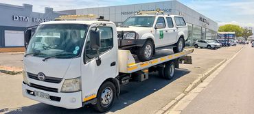 MHD Transport flatbed truck towing a white pickup in Cape Town, parked outside a dealership.