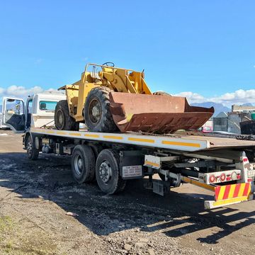 A yellow front loader is loaded on a flatbed tow truck under a clear blue sky.
