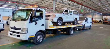 White MHD Transport truck loaded with 2 City fleet vehicles parked inside of a warehouse.