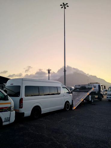 White MHD Transport truck loading a white Toyota Quantum.