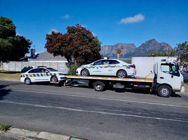 MHD Truck transporting 2 law enforcement vehicles at once under clear blue skies.