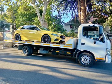 White MHD Transport truck standing in the road with a yellow Mercedez sports car on its deck.