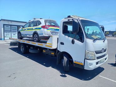 Tow truck carrying a SAPS police vehicle on a flatbed outside a transport depot in Cape Town.