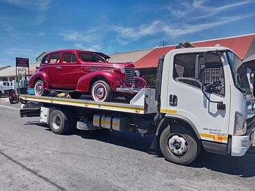 Flatbed tow truck transporting a restored red classic car in Cape Town under clear blue skies.