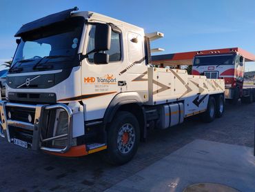 White Volvo flatbed truck parked under clear blue sky.
