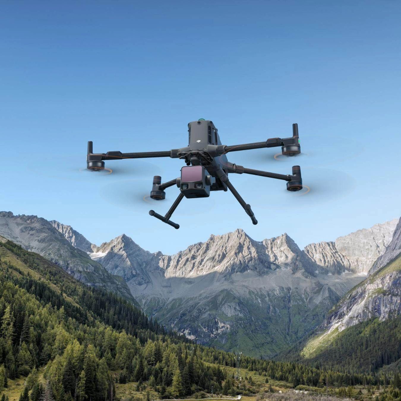 A drone flying over a mountainous forest landscape in British Columbia under a clear blue sky.